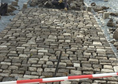 Das Foto zeigt zwei Pflasterer, die in Quedlinburg eine schmale Straße aus Kopfsteinen Pflastern. Fotografiert im Oktober 2010