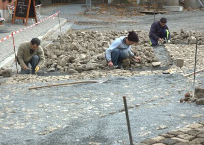 Das Foto zeigt drei Pflasterer, die einen Platz auf dem Burgberg in Quedlinburg mit unregelmäßigen Natursteinen pflastern - fotografiert im Oktober 2010