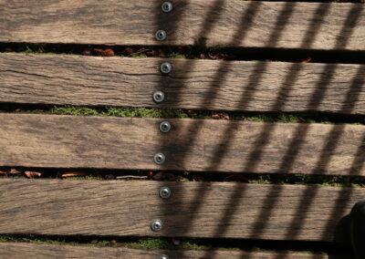 Das Foto zeigt schräge parallel Schatten der Geländerstäbe an einer holzbeplankten Brücke im Felsenmeer bei Hemer im Oktober 2024