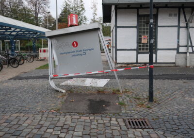 Das Bild zeigt einen aufgeständerten Stadtplan in Ratingen, der allerdings angefahren wurde und nun - völlig windschief - mit Absperrbändern versehen wurde. Fotografiert im November 2018