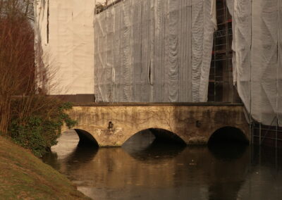 Das Foto zeigt Schloss Kalkum hinter dem Schlossgraben, verhüllt mit Gerüst und Planen im Januar 2019