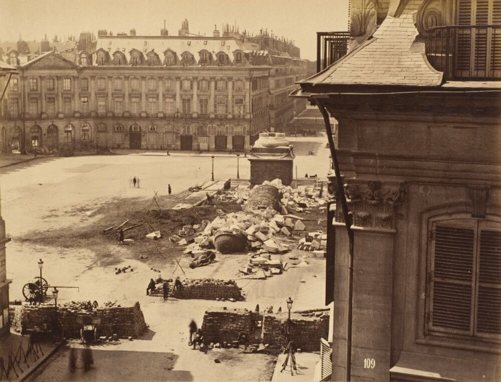 Place Vendôme nach dem Sturz der napoleonischen Siegessäule (am 16. Mai 1871). Vorn eine Barrikade der Pariser Commune, die nur wenige Tage später blutig niedergeschlagen wurde.