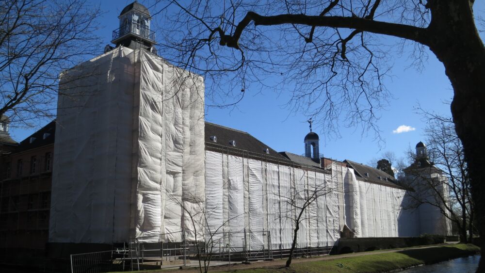 Da Foto zeigt das eingerüstete und mit weißen Planen verhüllte Schloss Kalkum vor blauem Himmel - im März 2018